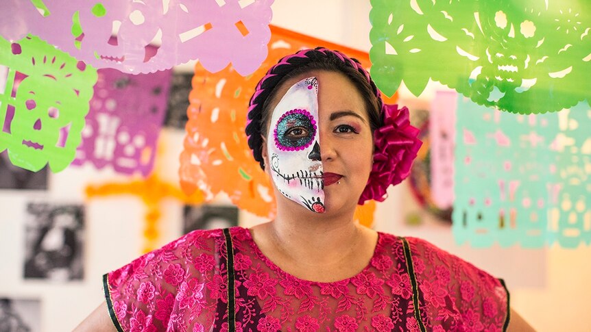 A woman with her face painted stands with a string of colourful stencils hanging around her.