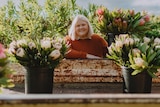 Nikki Davey wearing a red jumper stands behind potted flowers on a flower farm.