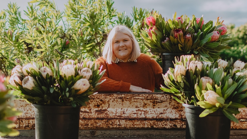 Nikki Davey wearing a red jumper stands behind potted flowers on a flower farm.