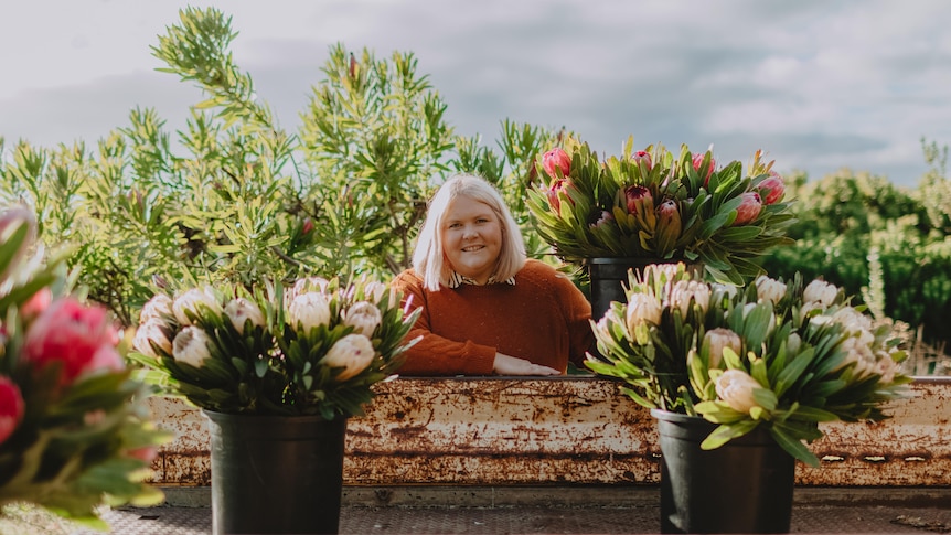 Nikki Davey wearing a red jumper stands behind potted flowers on a flower farm.