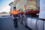 man in high viz and beanie leans against truck carrying hay for drought affected farmers.