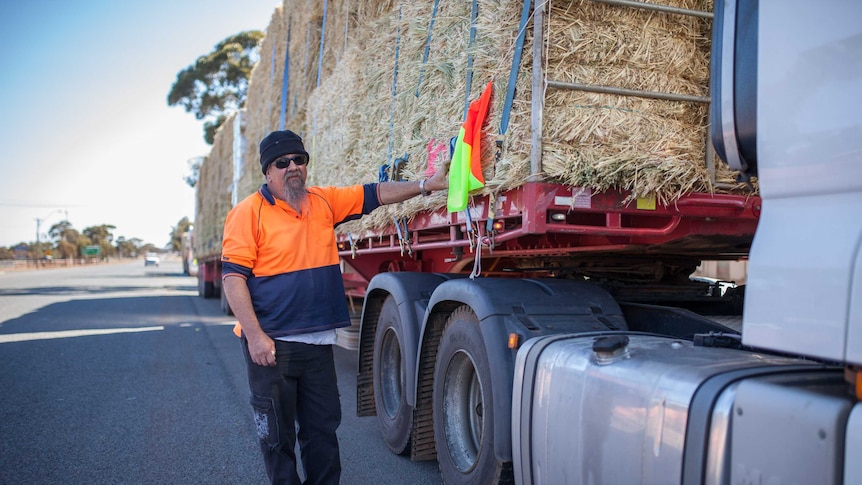 man in high viz and beanie leans against truck carrying hay for drought affected farmers.