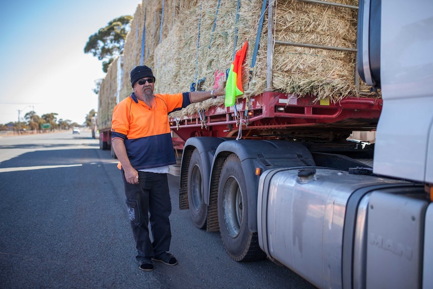 man in high viz and beanie leans against truck carrying hay for drought affected farmers.