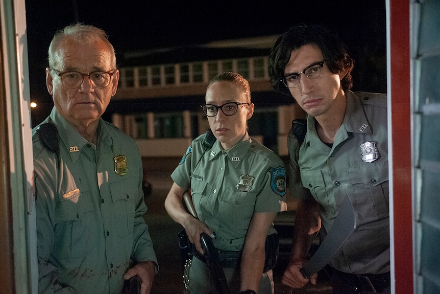 Two male and one female police officers stands in doorway holding weapons at night time.