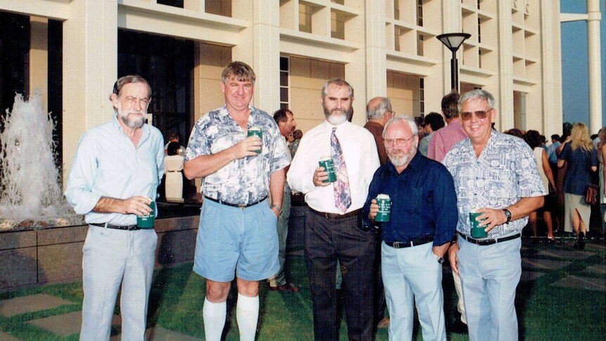 Five men stand with beers outside of parliament .