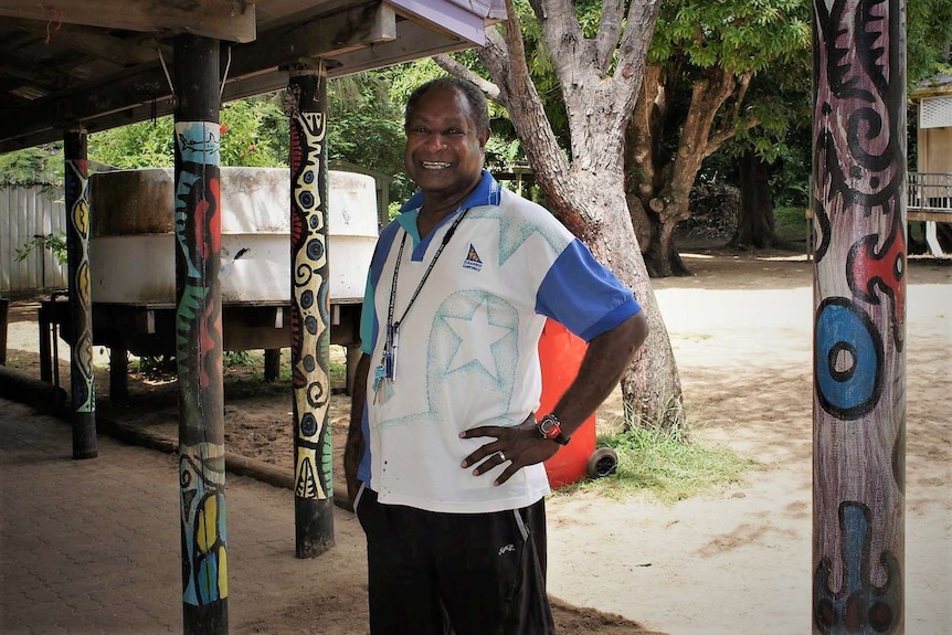 Torres Strait Islander man smiling with painted timber poles in background
