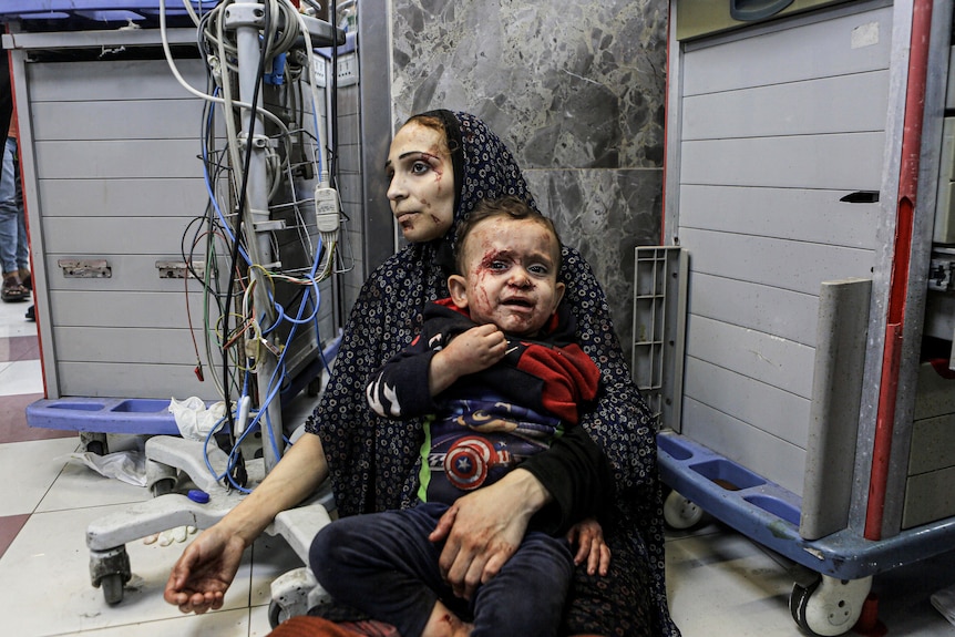 Mother holds child in front of hospital equipment as child cries