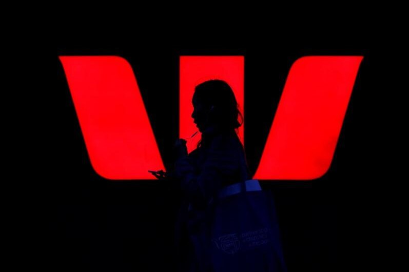A woman walks past an illuminated logo for Australia's Westpac Bank in Sydney