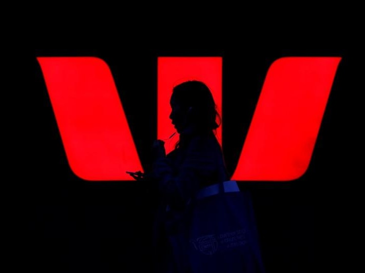 A woman walks past an illuminated logo for Australia's Westpac Bank in Sydney.