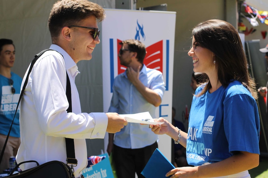 young liberal woman, dressed in blue campaign t shirt, hands leaflet to young man