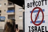 A white wall shows a boycott israel stencil with a red mark over the israeli flag