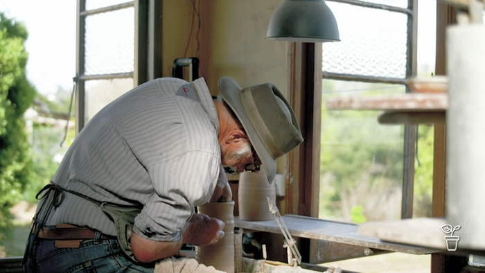 Man in hat working on pottery in a shed outlooking a garden