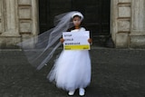 A young girl wearing a white wedding dress holding a placard saying 'Stop Child Marriage'