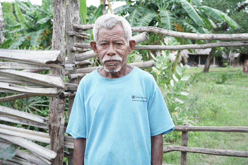 An old man in a blue t-shirt in a rural setting 