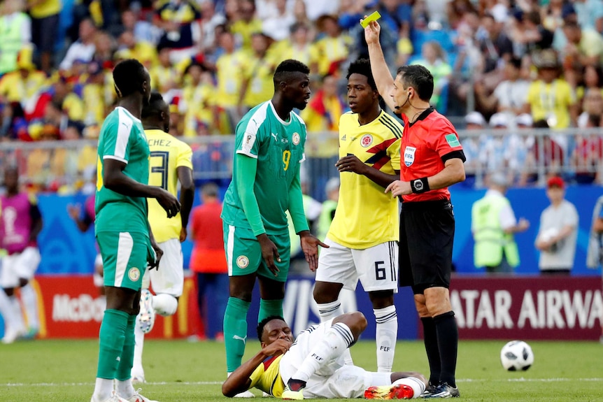 Referee Milorad Mazic shows Senegal's M'Baye Niang a yellow card.