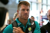 Cricketer David Warner looks serious as he walks through Cape Town International Airport surrounded by media