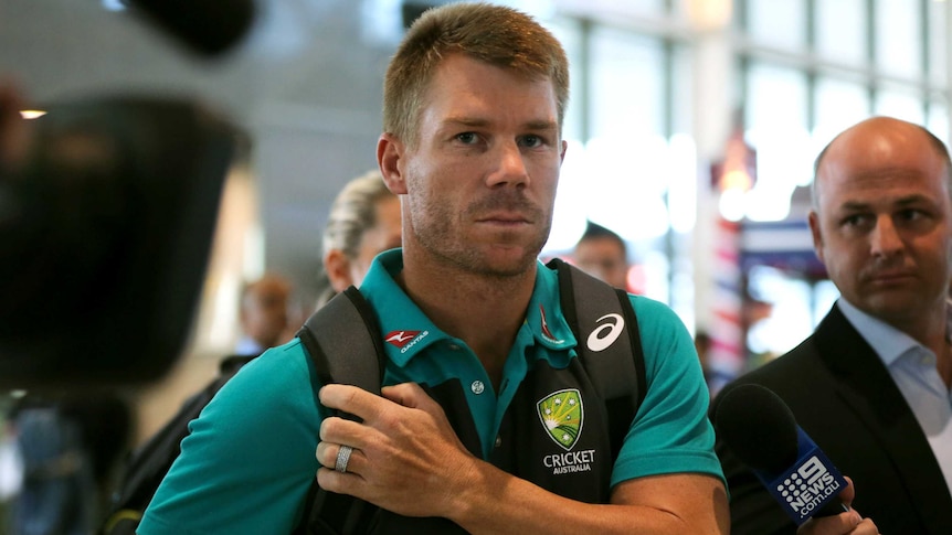 Cricketer David Warner looks serious as he walks through Cape Town International Airport surrounded by media