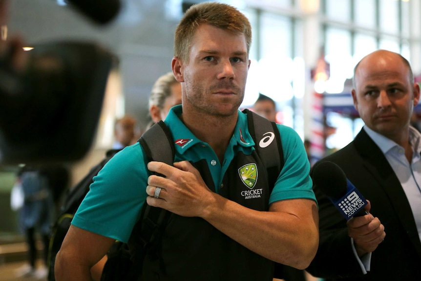 Cricketer David Warner looks serious as he walks through Cape Town International Airport surrounded by media