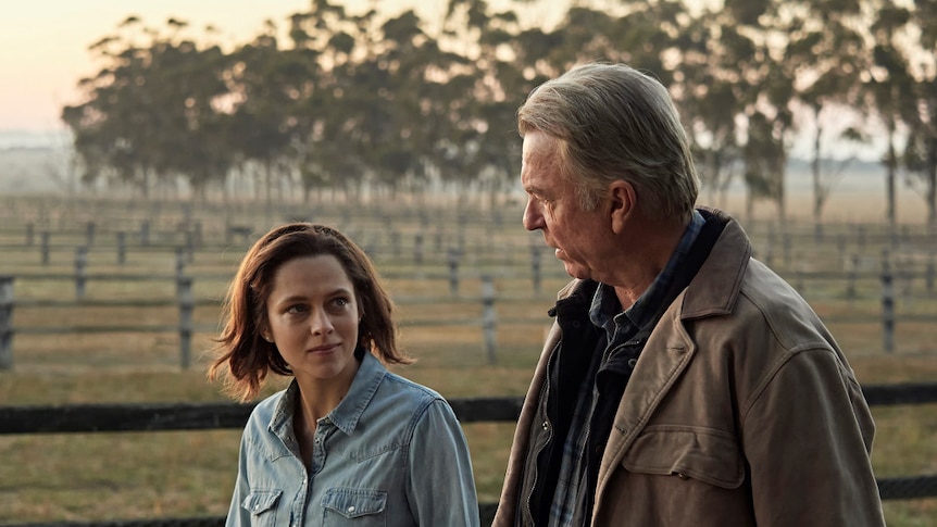 A short young woman and her father are talking in a still from a film.