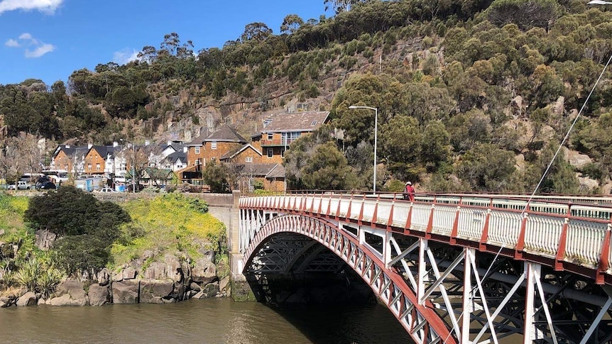 Historic steel bridge over a river, looking towards stone buildings on the other side of the river