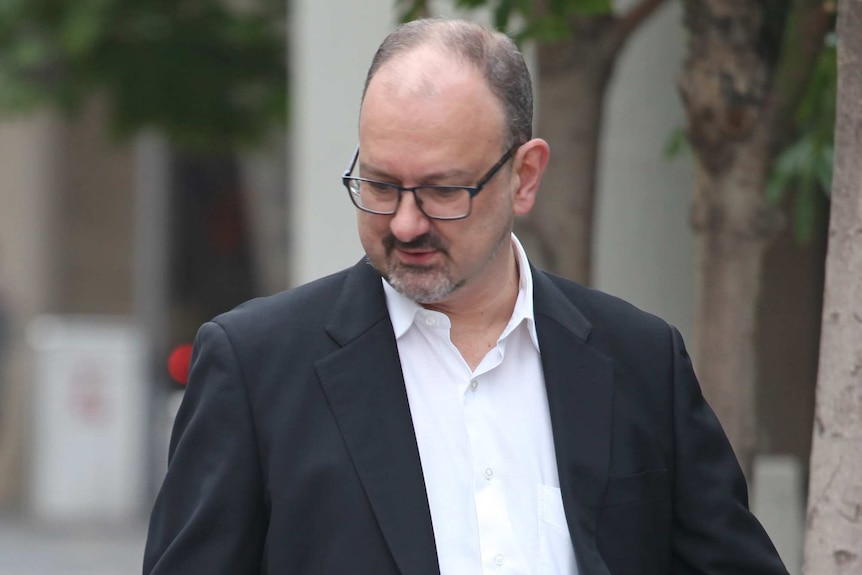 A mid-shot of Claremont serial killings trial defence lawyer Paul Yovich walking outside wearing a black suit and white shirt.