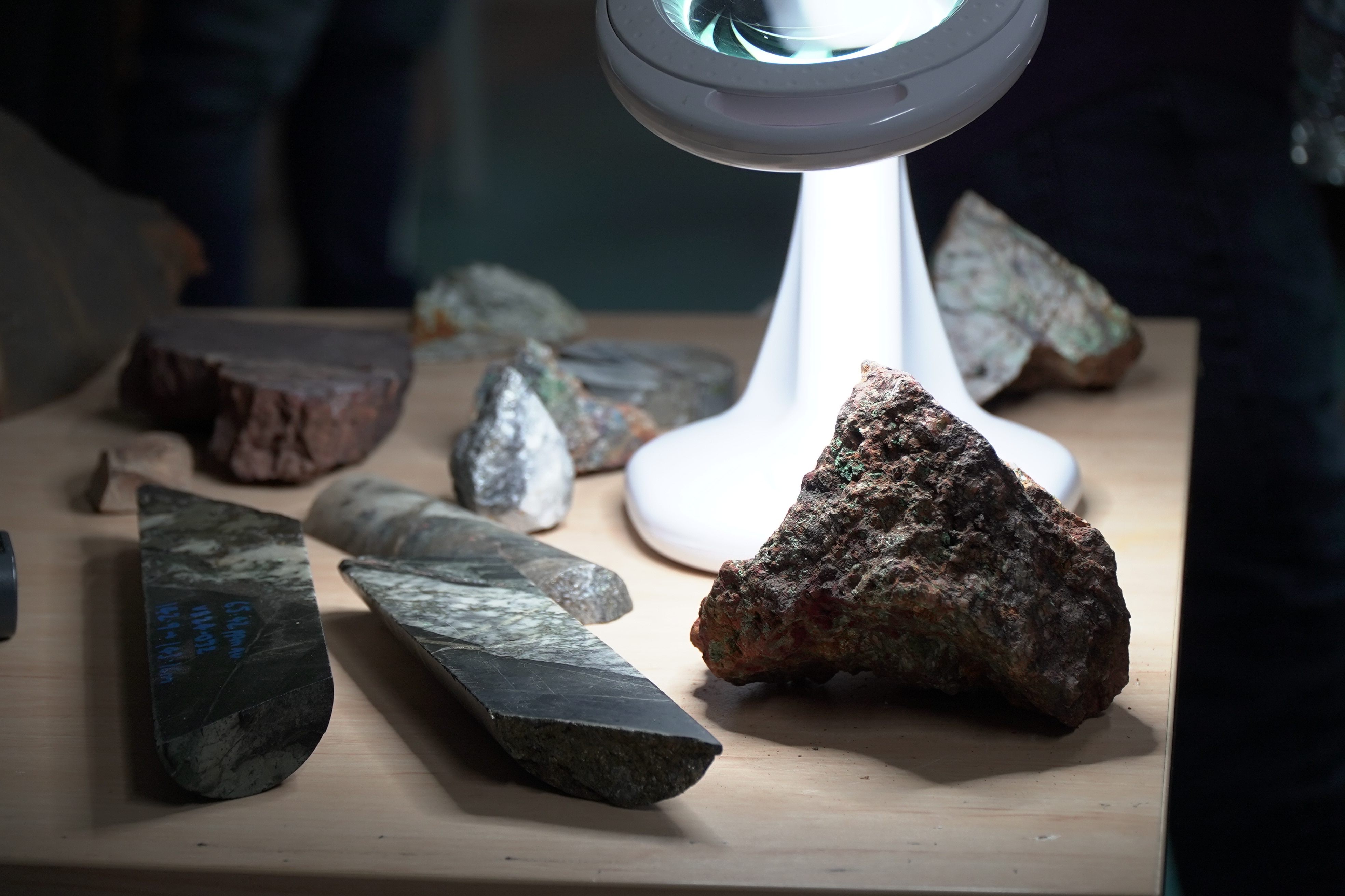 Half-a-dozen rocks sitting on a wooden table, all different sizes an types, lit by a magnifer and its built in light.