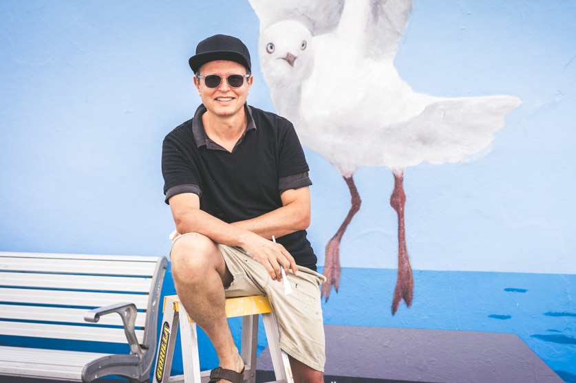 Andre Braun in front of a painted mural of a seagull at the promenade graffiti wall at Bondi Beach.