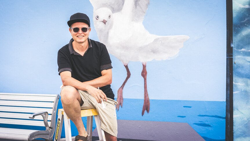 Andre Braun in front of a painted mural of a seagull at the promenade graffiti wall at Bondi Beach.