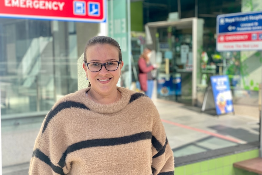 A woman wearing glasses smiles outside a hospital.