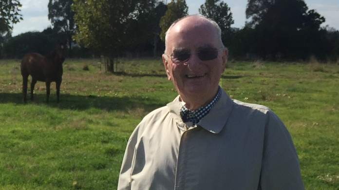 Am older man stands on a farm with two horses.