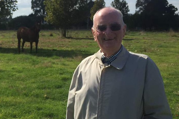 A man stands on a farm with two horses.