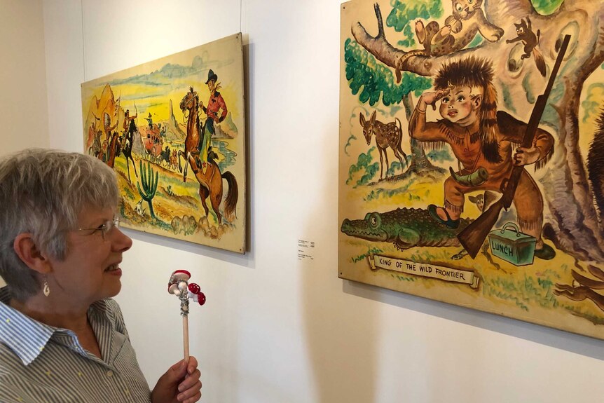 A lady looks at colourful paintings in an art gallery, depicting scenes from children's stories.