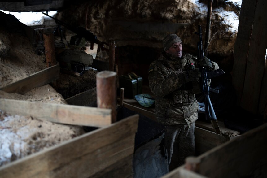 A soldier holds a gun in a dim-lit underground trench. 