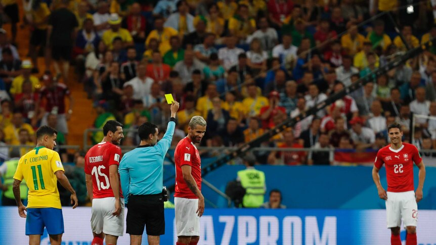 Referee shows Swiss player a yellow card while Neymar lies on the ground
