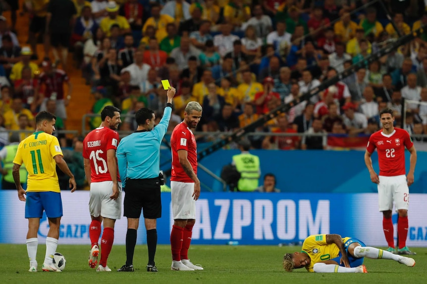 Referee shows Swiss player a yellow card while Neymar lies on the ground