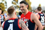 A Melbourne Demons ruckman smiles as he talks to a teammate (whose back is turned to the camera) after a win.