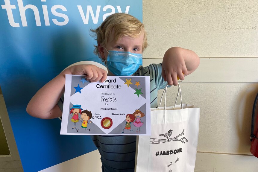 A nine-year-old boy holding a certificate and a show bag saying "jab done"