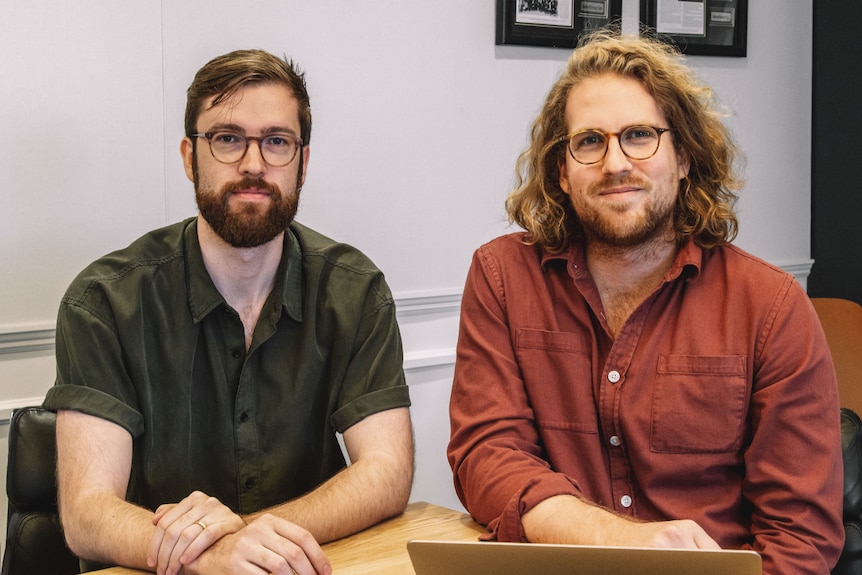 Two young men, both in glasses, sitting at a desk