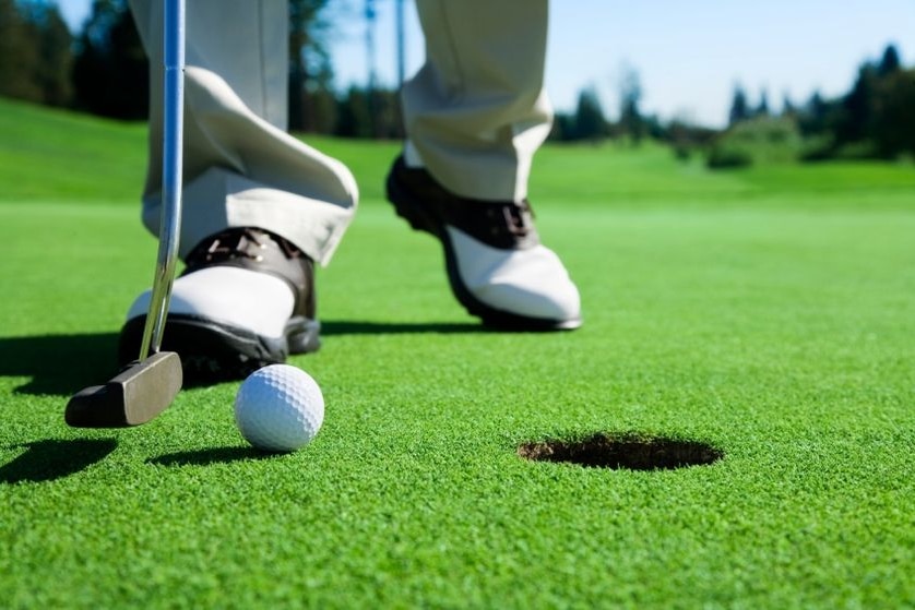 A golfer stands close to a hole about to putt the ball in.