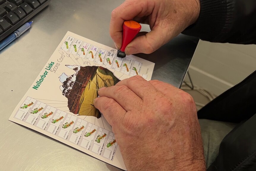 Close up of a man's hands stamping a scorecard with map of Australia and ticked boxes