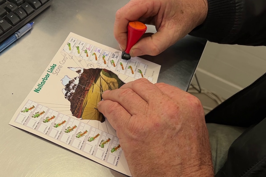 Close-up of a male hand stamping a scorecard with a map of Australia and a check box