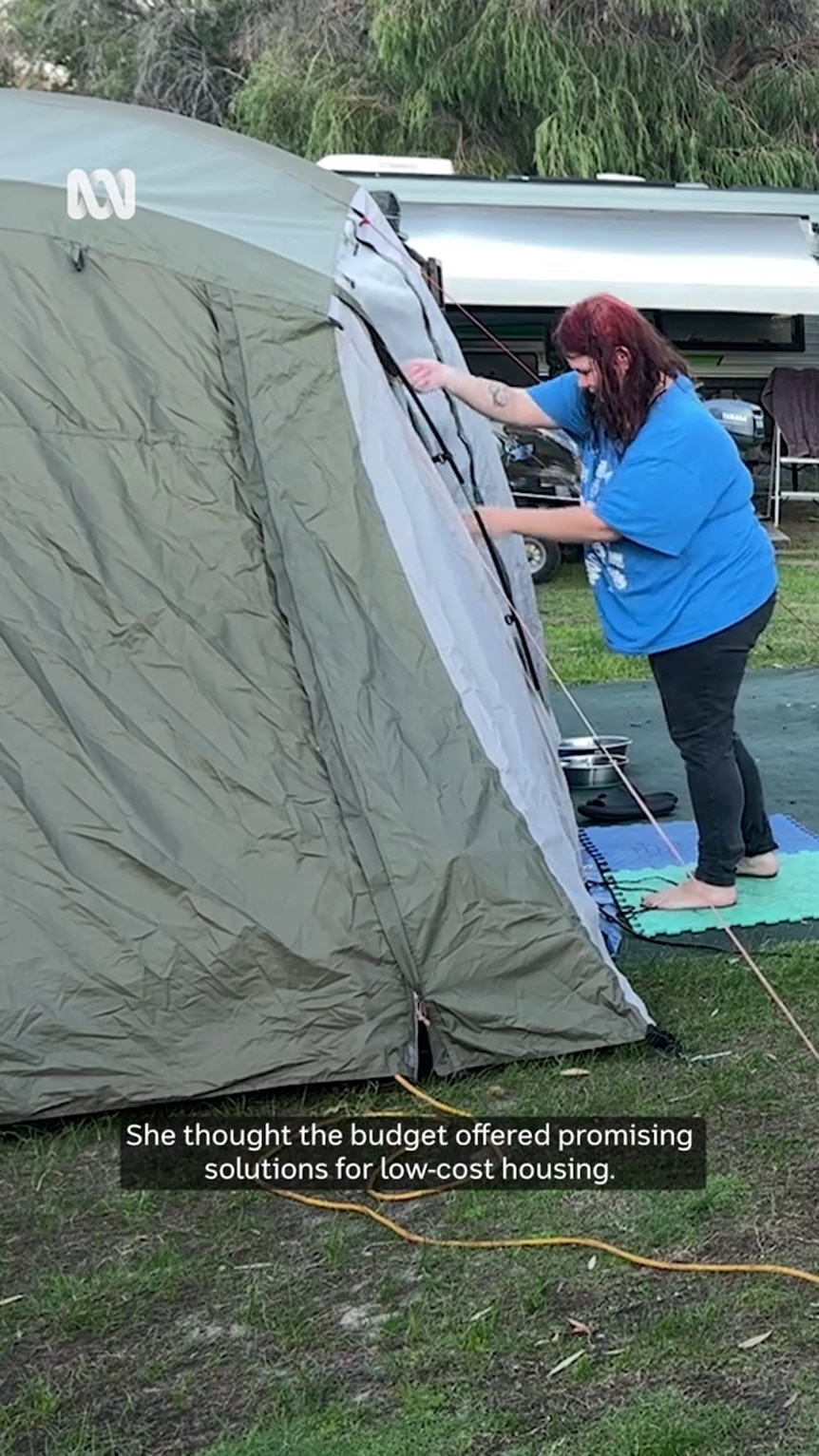 A woman in a large blue t-shirt reaches towards a tent 