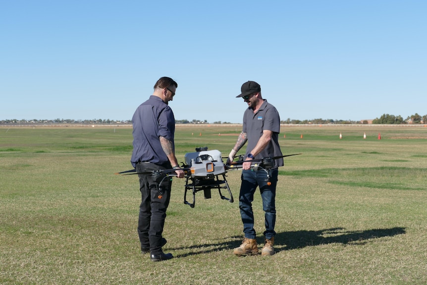 Two men holding a large drone in a green field