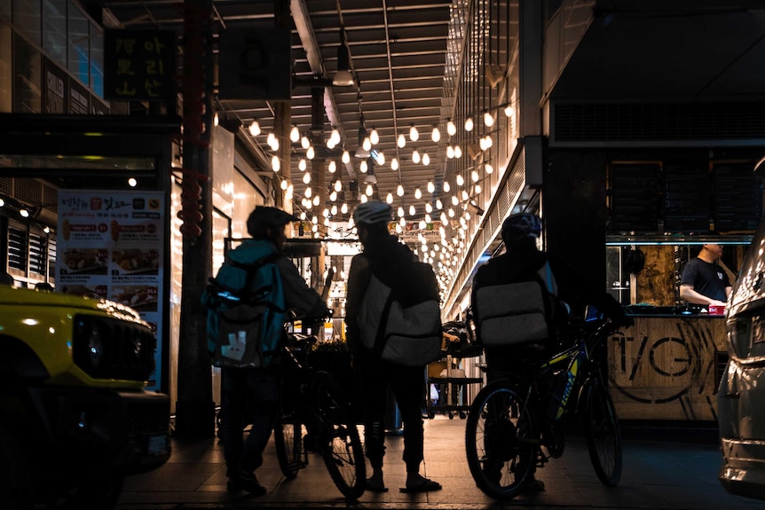 Three men on bicycles looking into a mall.