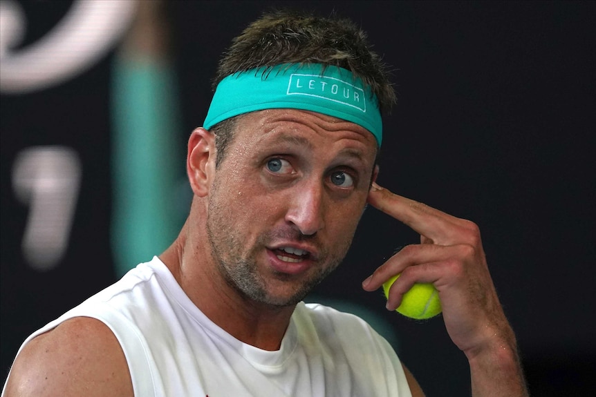 Tennys Sandgren holds a tennis ball and points to his head during an Australian Open match against Roger Federer.