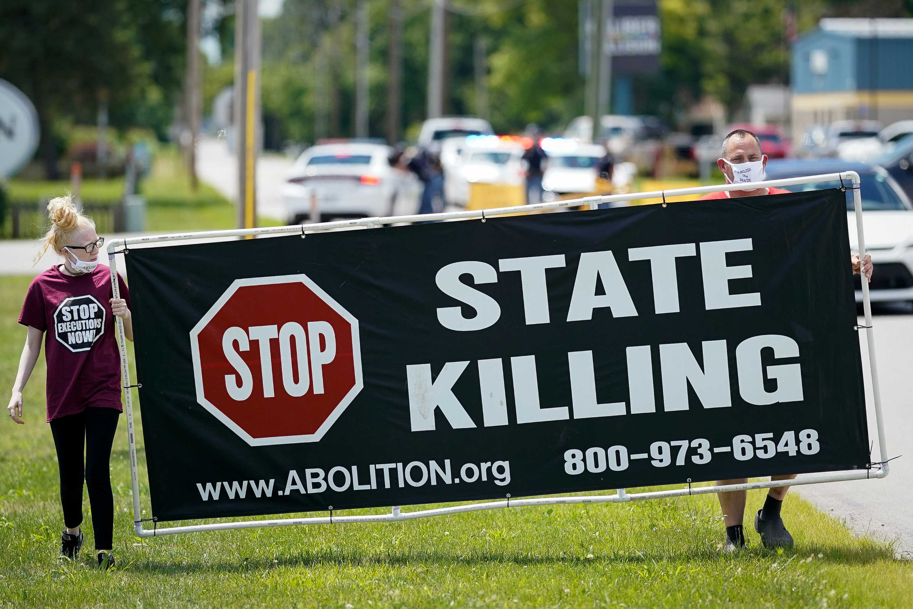 一个女人和一个男人举着一个标语，上面写着“停止国家杀”。 class=