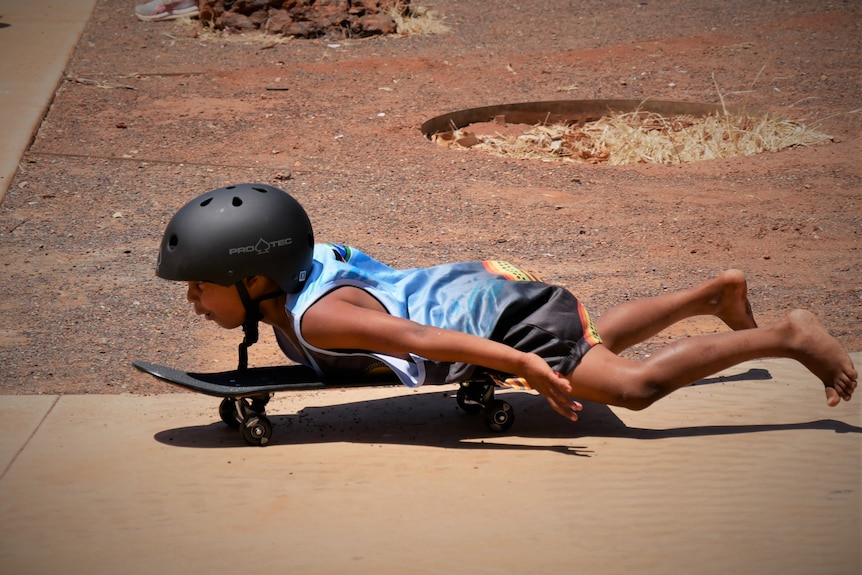 A kid lays on a skateboard and glides along. 