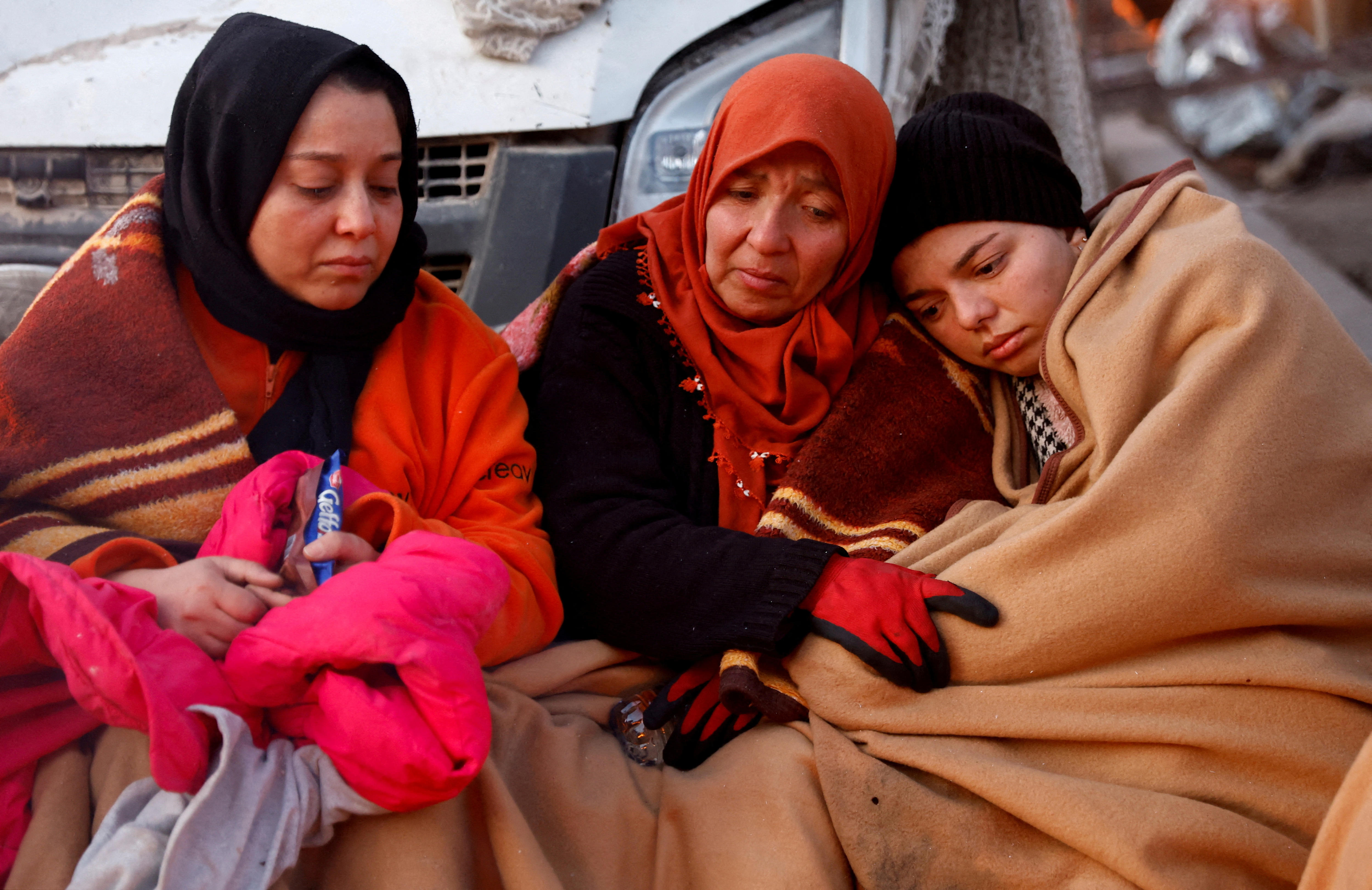 People rest on a street next to rubble and damages near the site of a collapsed building in the aftermath of an earthquake