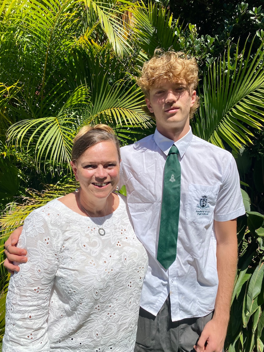 Leanne smiles and puts her arm around her son, who is wearing a collared school uniform and green tie.