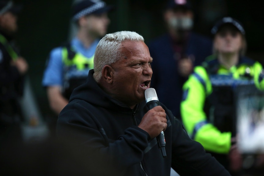 A man with white hair yells into a microphone.